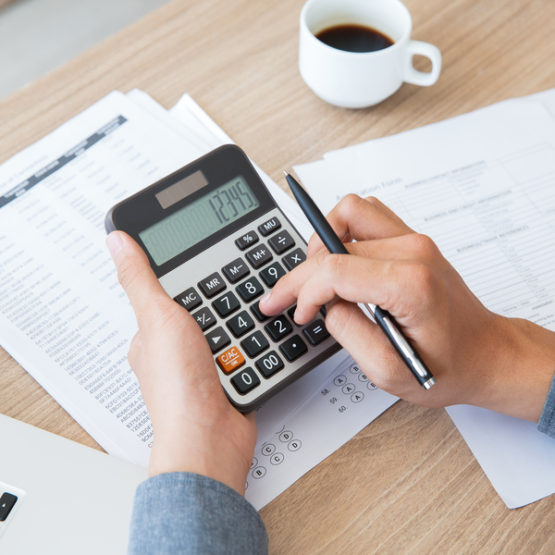 Man using calculator to count income and outcome Unrecognizable businessman using calculator to find out income and outcome. He counting company finances. Male hands with pen pushing button at desk. Investment or paperwork concept